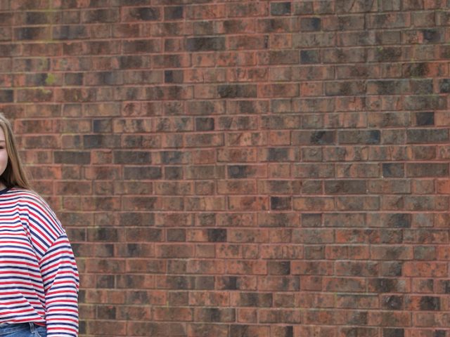 cassidy stands in front of a brick wall.