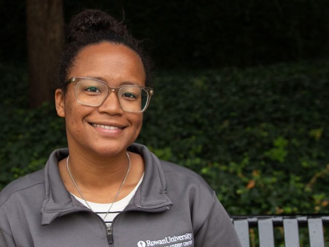 Autumn Vilches-Cruz, junior Psychology major, sitting on a bench outside on Rowan's campus