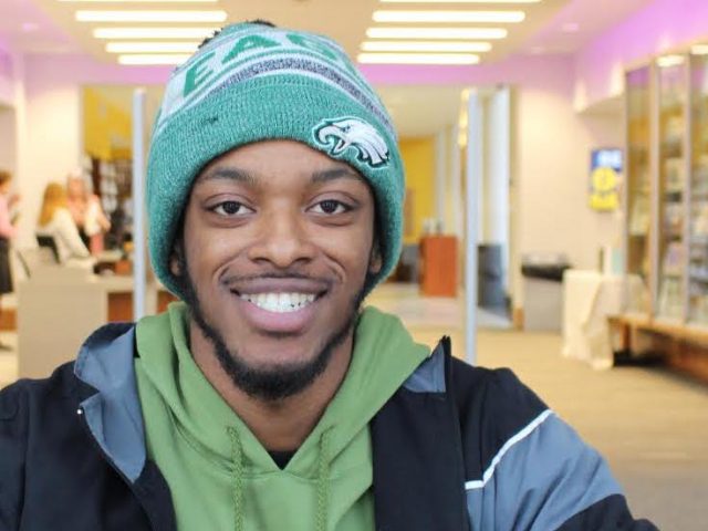 Jamal sitting in the library with a green beanie on.