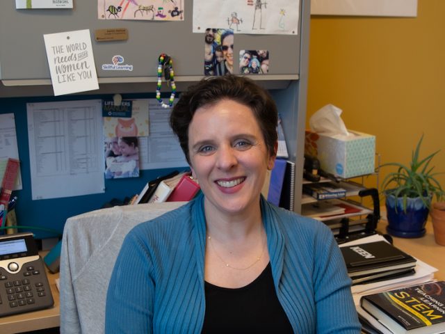 Professor sits at her desk, hands clasped