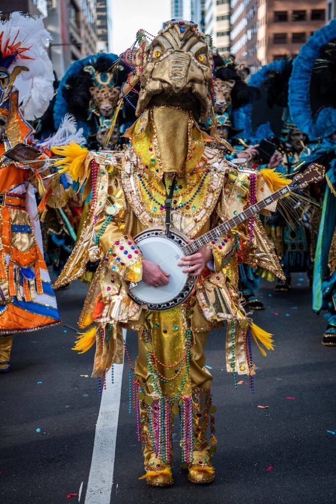 A fully costumed TJ wearing a large headpiece and outfit made of feathers, while playing a banjo.