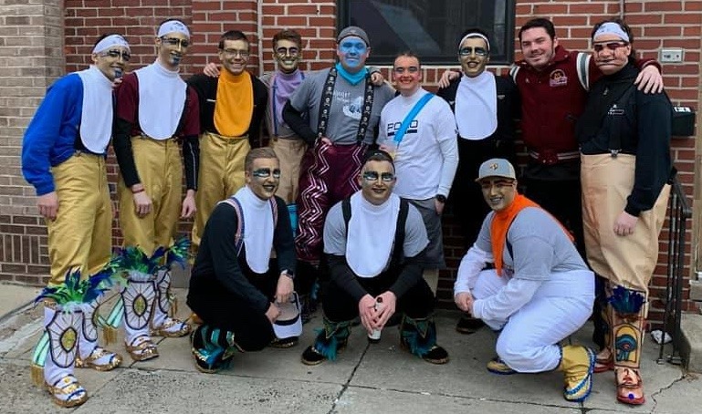 Twelve men dressed in partial Mummers costumes and makeup pose together for a portraight outside.