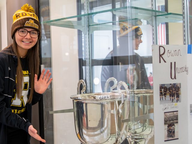 Emily stands in front of the women's ice hockey trophy.