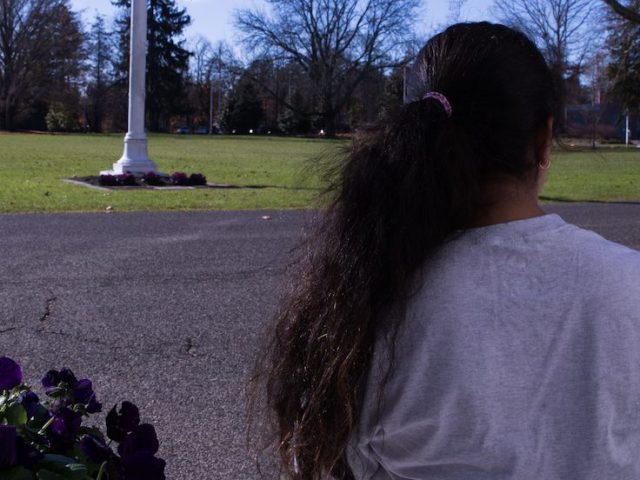 Girl stares into the distance as we see the back of her head and ponytail.