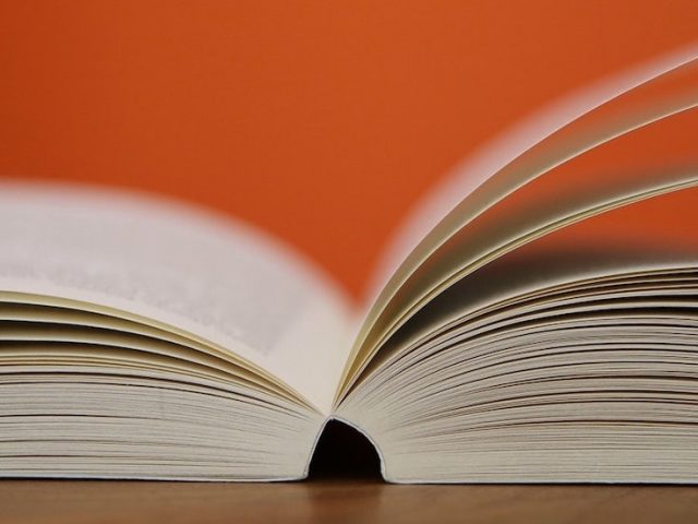 Stock image of an open book fanned against an orange background.