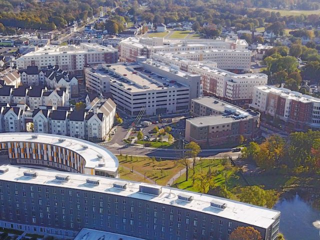 Drone view of Holly Pointe curved building with trees in the horizon.