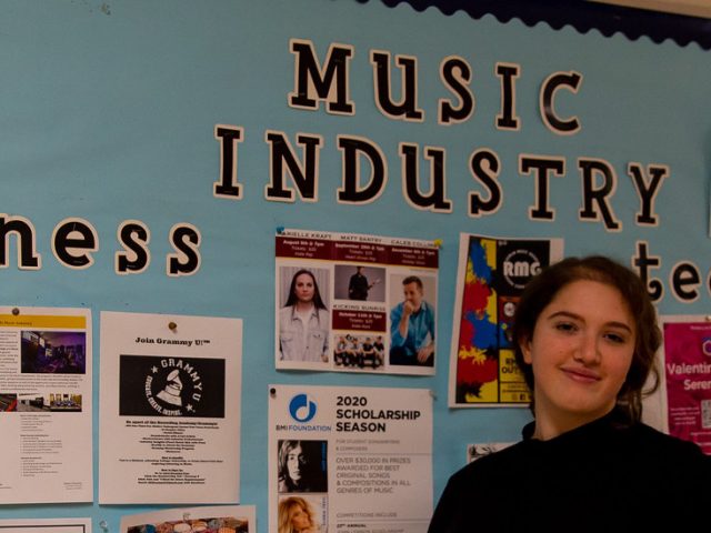 Bianca stands in front of a Music Industry bulletin board.