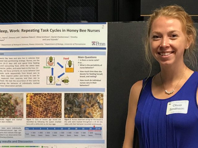 Olivia stands in a blue tank top next to a poster during a presentation.