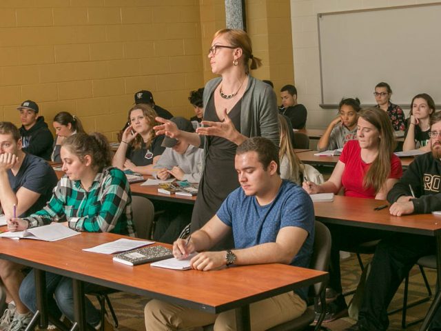 a yellow and white classroom full of students sitting at rows of desks.