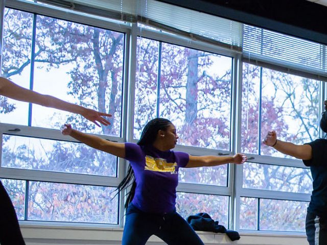 students dancing in a bright room with windows.