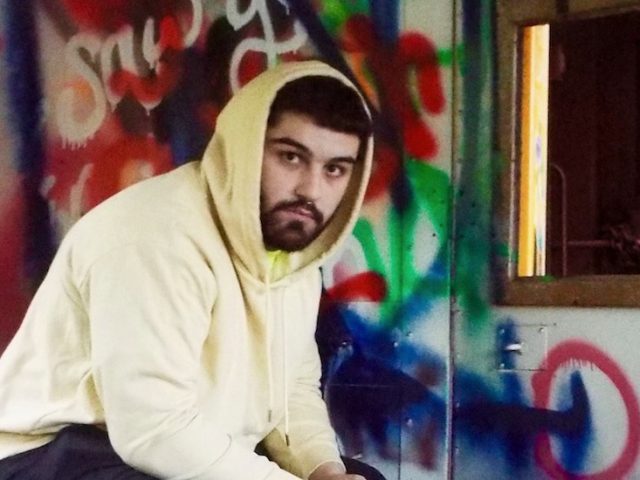 Photo of Frank Ziegler wearing a hooded sweatshirt sitting in a graffiti-covered room