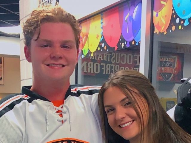 A close up of George wearing an ice hockey uniform, standing close to a young woman.