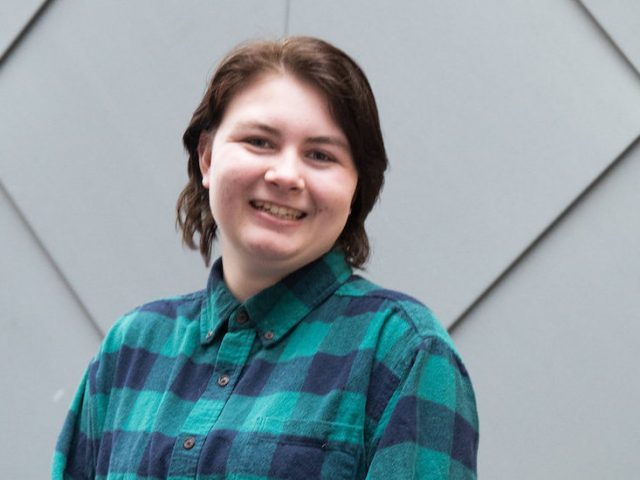 Marissa poses for a portrait while wearing a green plaid shirt.