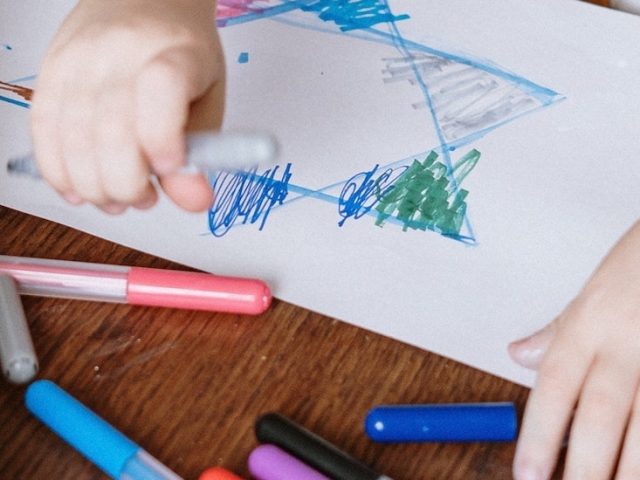 Stock image of close up of adult hands guiding child's hands drawing.