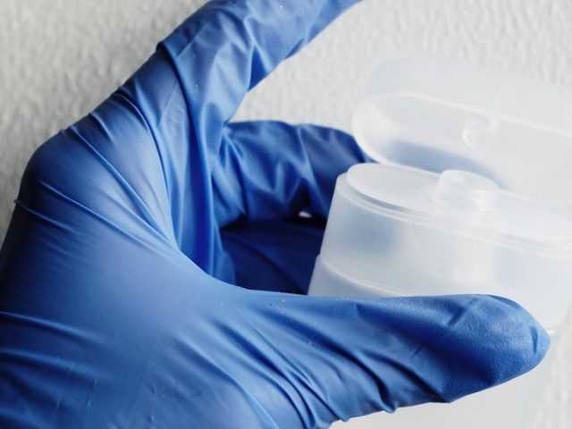 Stock photo of a hand covered with a blue medical glove holding a plastic container.