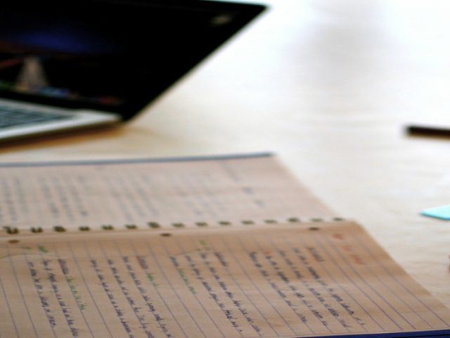 A stock image of a laptop and a notebook with pens