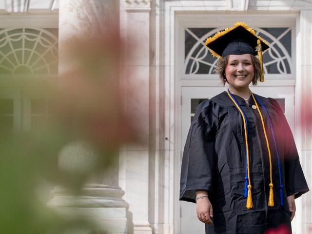 Chelsey Fitton stands in her cap and gown outside of Bunce Hall