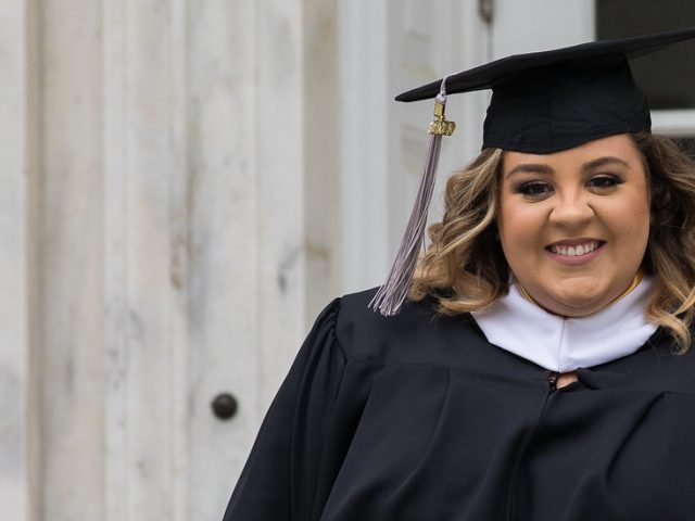 Megan Pfizenmayer stands outside of Bunce Hall in her cap and gown