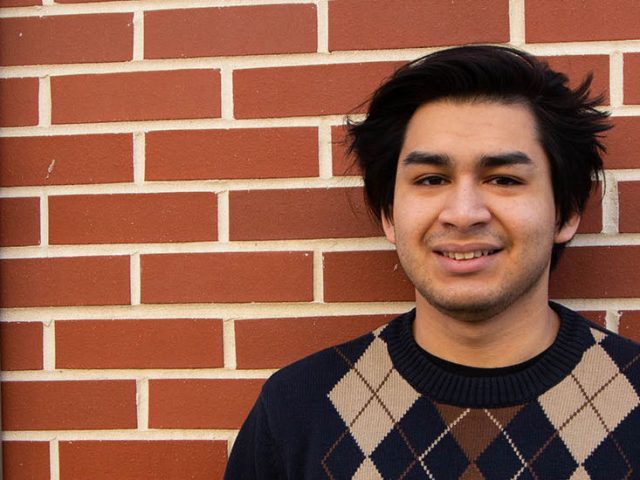 Enzo stands against a brick building on campus