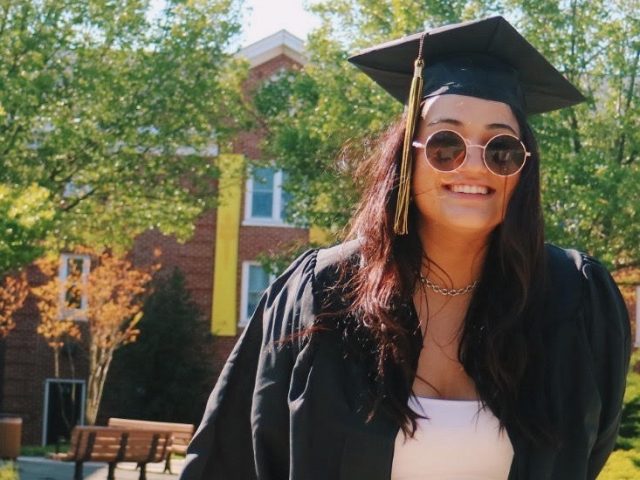 Gianna poses in front of a freshman residence hall in her graduation regalia.