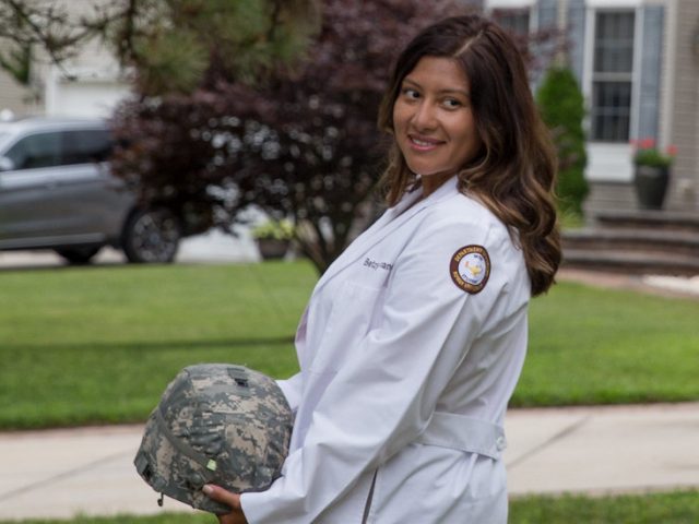 Betzy looks at a distance holding her military helmet.