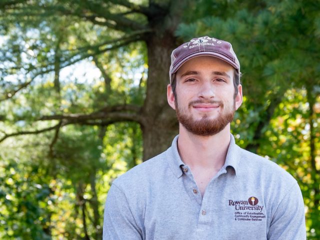 Will sits among pine trees on campus.