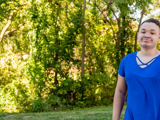 Christine standing outside in front of trees in a blue shirt.