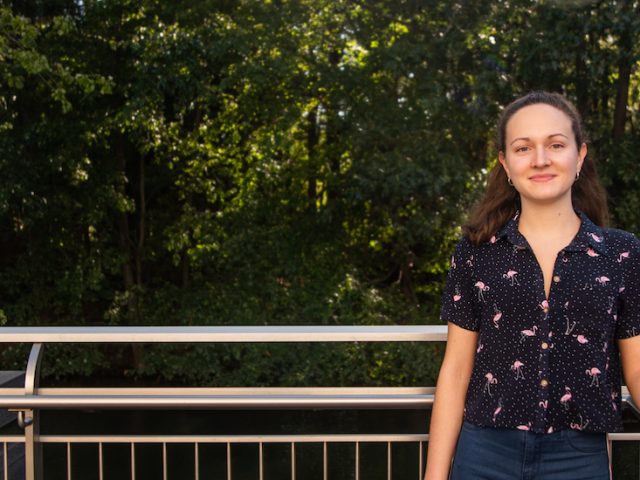 Jennifer stands outside by a wooded area of campus.