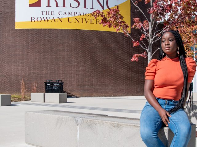 Nafisat Olapade sitting on a cement bench in front of a large brick building.