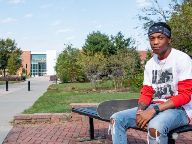 McCarly sits on a bench on campus outside.