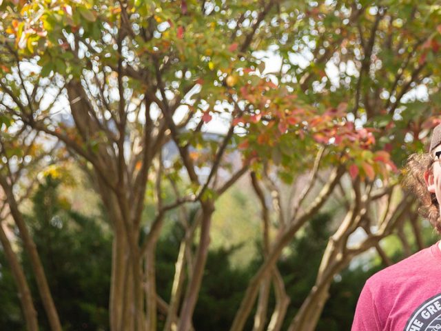 Griffin poses in a backwards hat in front of orange and green trees.