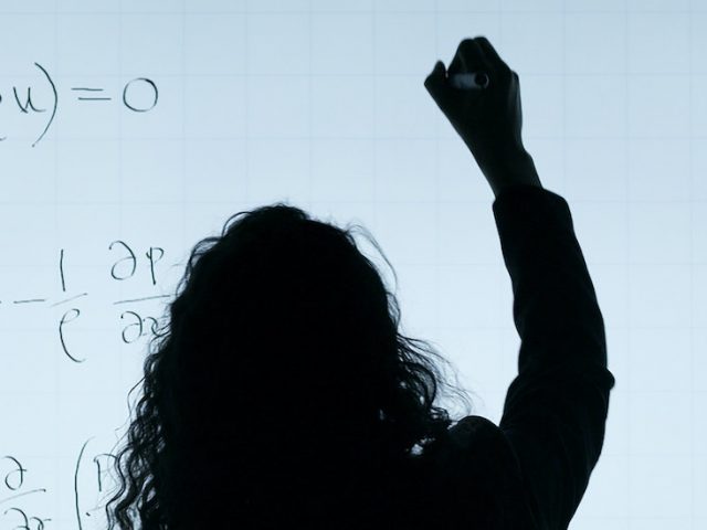 Backlit image of woman writing on a white board.