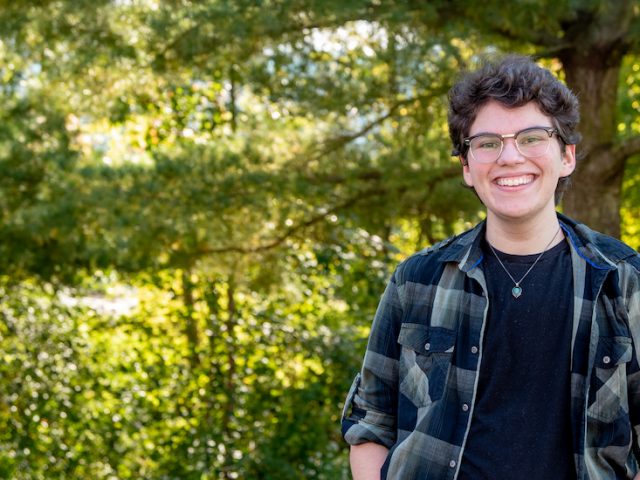 Elliot stands in a wooded area on campus.