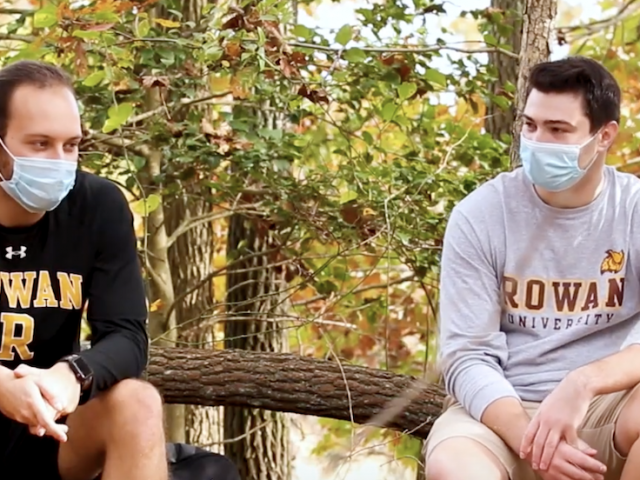 Two students in Rowan gear sit at the nature preserve.