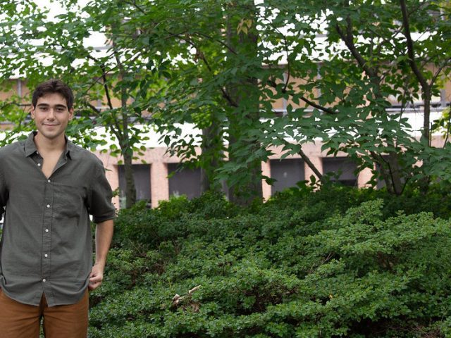 Marco stands in a wooded section of campus.