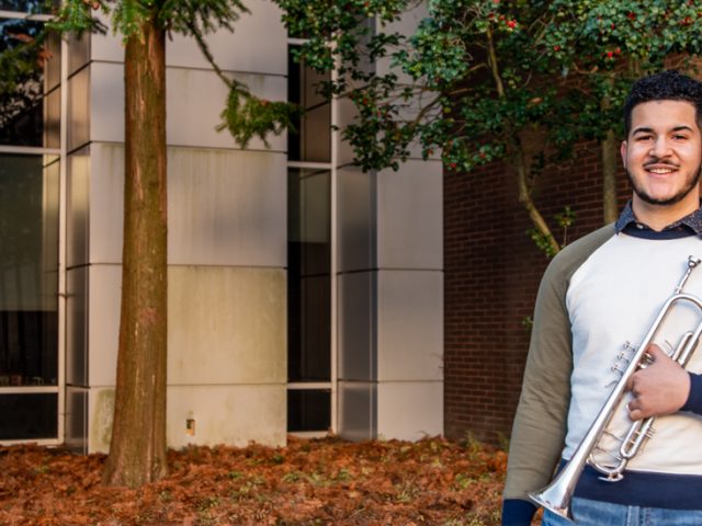 Luis standing outside of WiIlson hall with his trumpet.