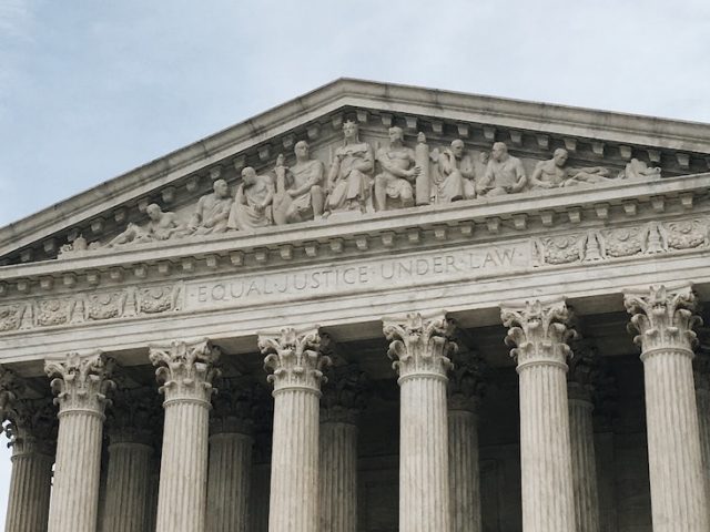 A close up of marble columns at the top of a traditional looking state building.