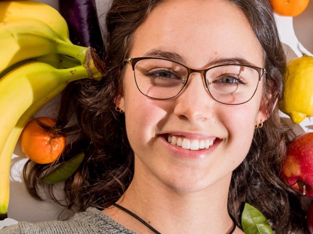 Close of Hannah's face surrounded by fruit.