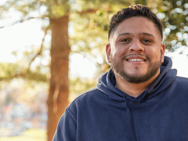 Martin Gonzalez sits by trees on campus.