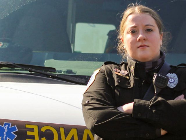 Maribeth stands in front of an EMT vehicle.