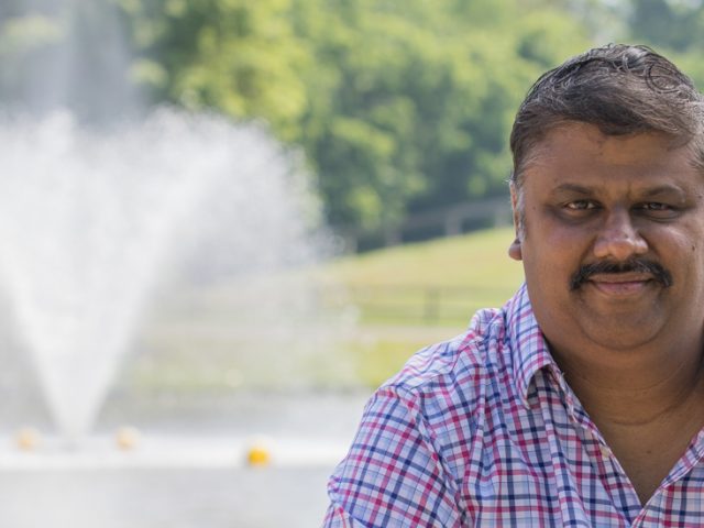 Ganesh smiles in front of a park area.