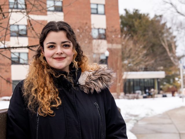 Mikayla standing at the bridge near the student center with snow behind her.