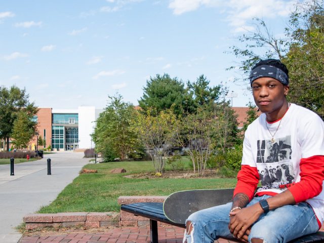 McCarly sits on a bench outdoors on campus.