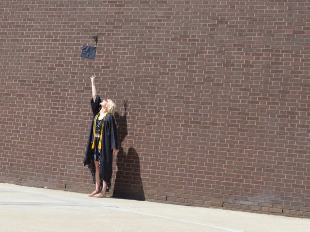 Amanda wears a cap and gown in front of a brick building.