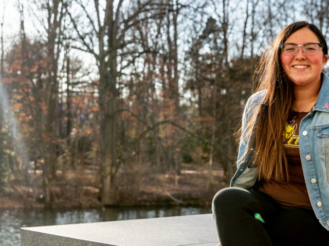 Giavana sitting on a stone near the engineering building with trees behind her.