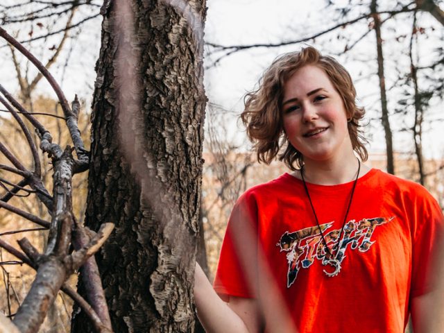 Victoria standing outside near some branches.