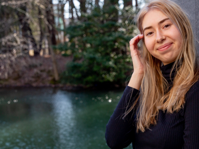 Madelaine poses against a wall next to a pond.