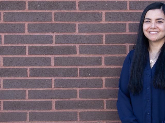 Holly stands against a brick wall.