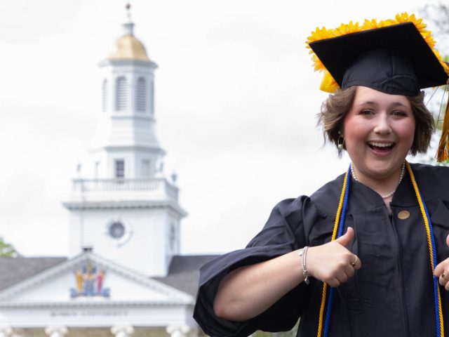 Student with cap and gown in front of Bunce.