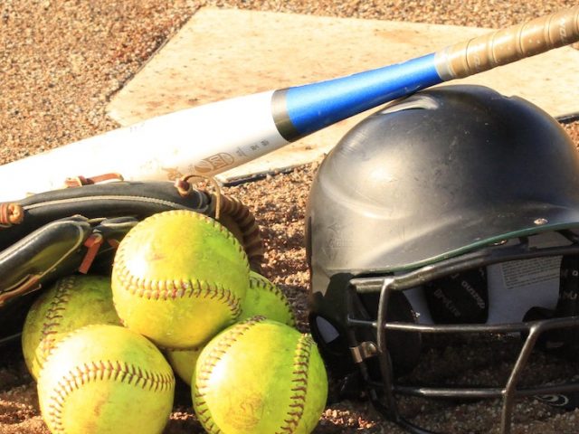 Stock image of a softball home plate with a helmet, three softballs and a bat.